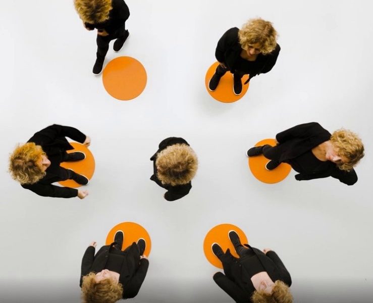 6 Personen stehen im Kreis und eine Person in der Mitte