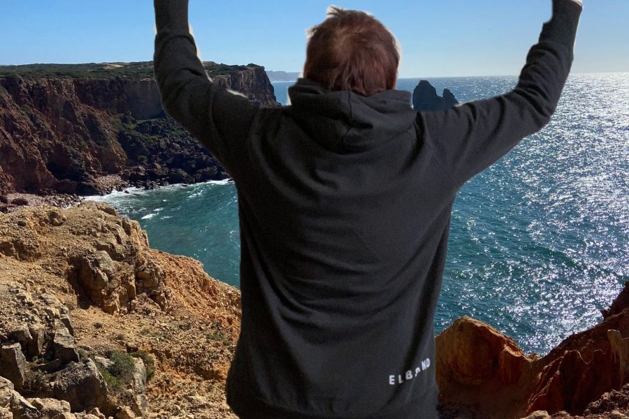 Frau Rücken sichtbar, breitet ihr Arme nach oben aus. Im Hintergrund ist das Meer zu sehen